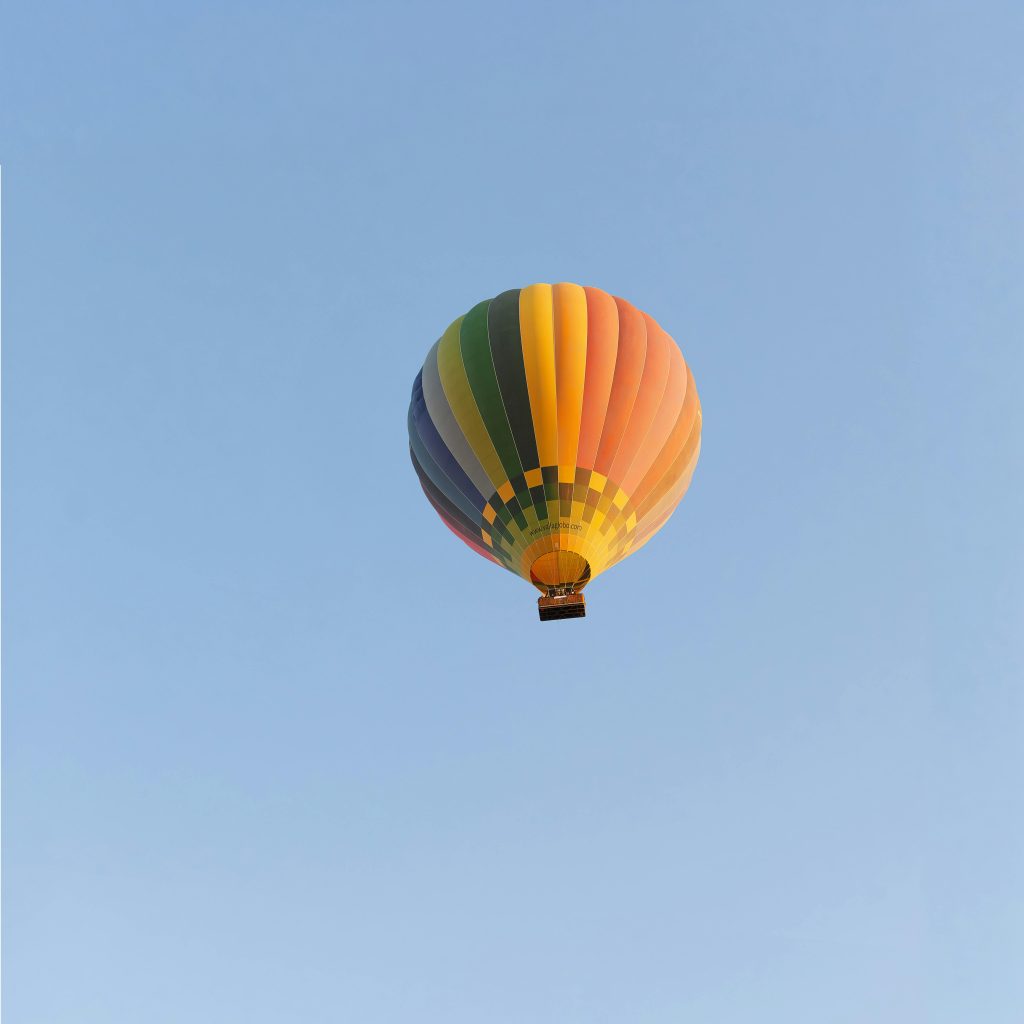 Vibrant hot air balloon soaring over Valladolid, Spain under a clear blue sky.